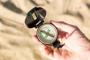 Male hand with compass on sand background.